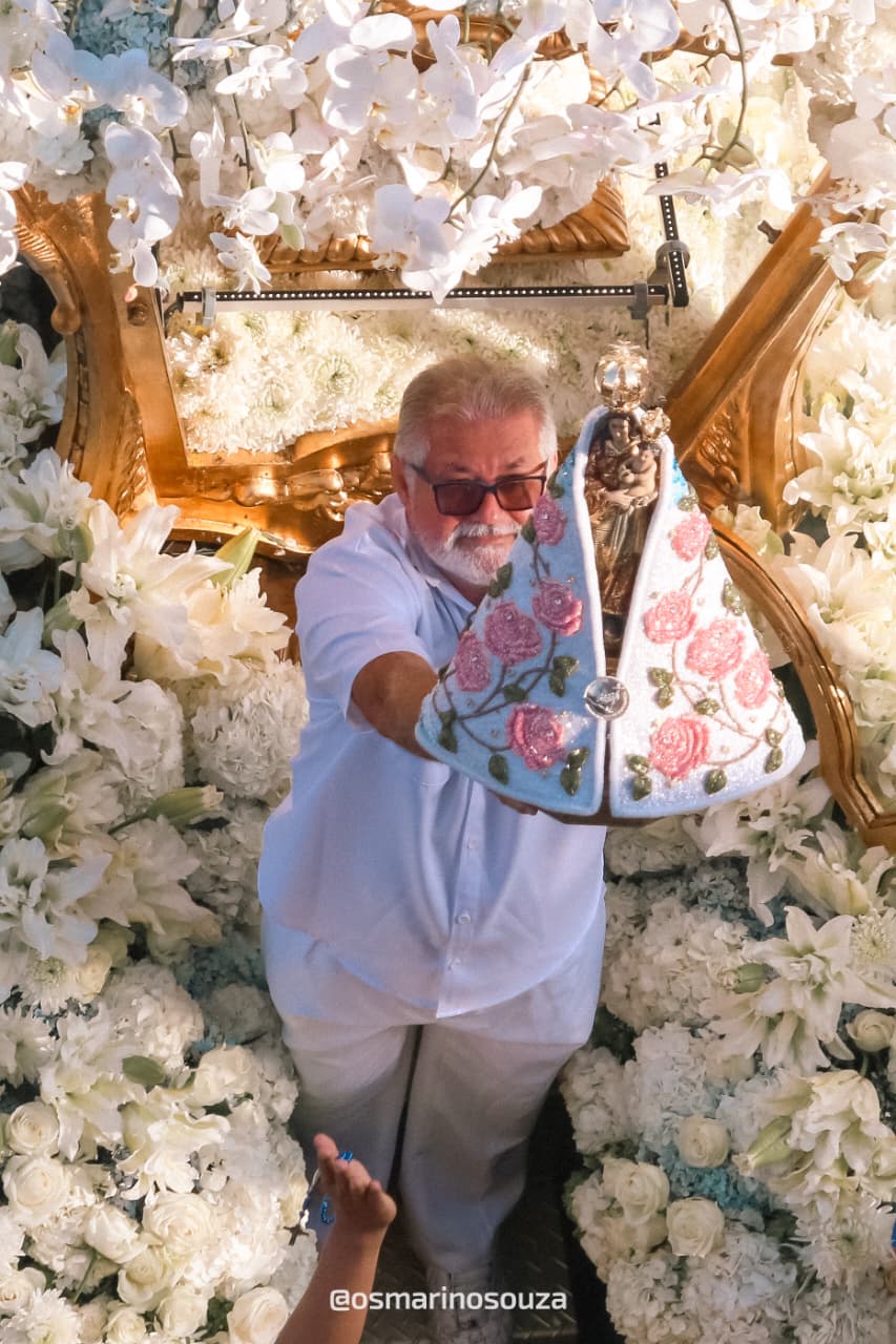 Devoto de branco estende a imagem de Nossa Senhora de Nazaré do alto da berlinda coberta de flores brancas durante o Círio em Belém