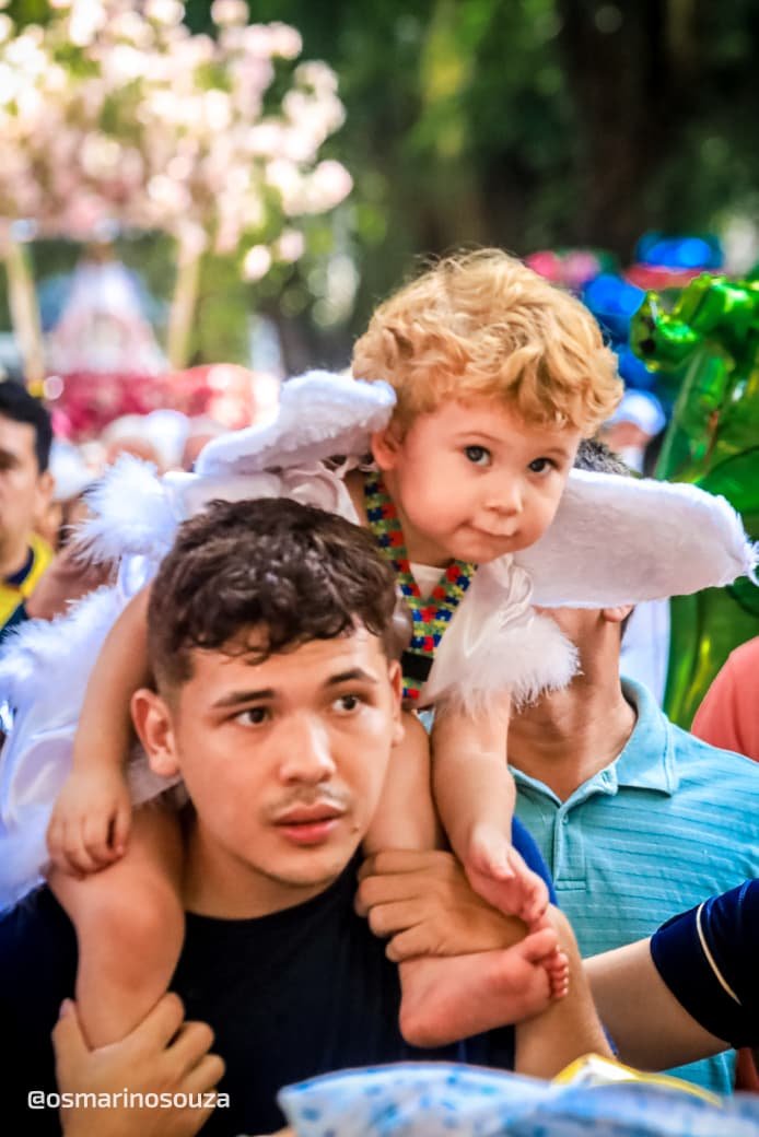 Jovem leva nos ombros uma criança vestida de anjo durante o Círio