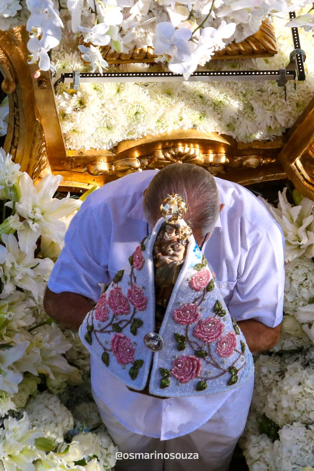 Devoto debruçado sobre a Imagem Peregrina entre flores brancas na berlinda