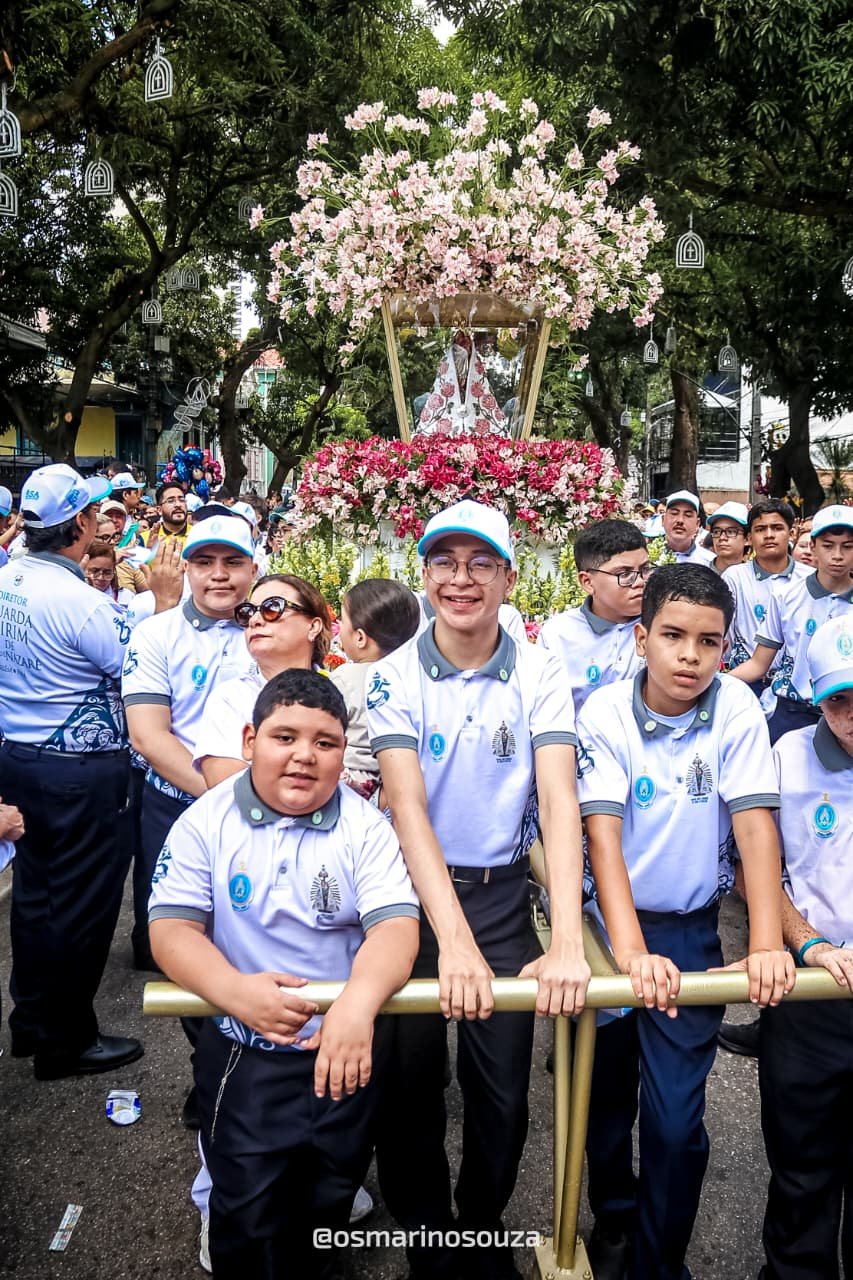 Estudantes de uniforme azul e branco diante de um andor florido