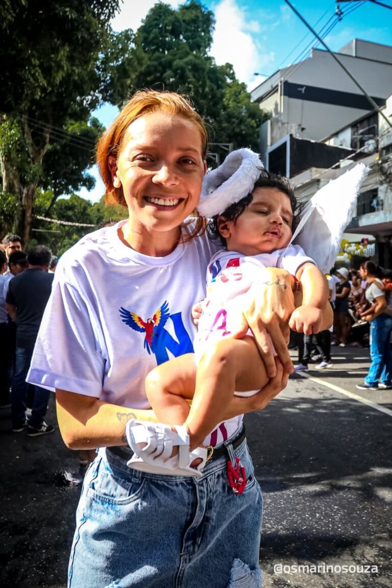 Mulher sorri com uma criança vestida de anjo no colo durante o Círio